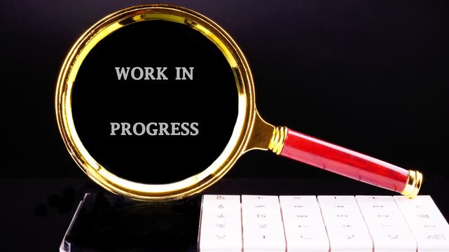Animated WORK IN PROGRESS text, viewed through a magnifying glass with a gold rim and red handle, against a black background.