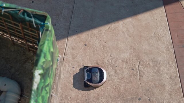 Compact robot vacuum cleaner rolling independently on outdoor tiled street surface viewed from above, comic machine rebellion concept,  robot uprising humor, autonomous device lifestyle.