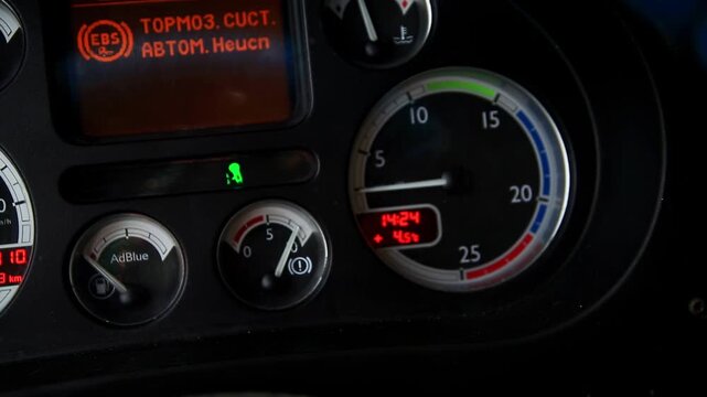 Detailed perspective of truck instrument cluster, featuring tachometer, AdBlue gauge, temperature dial, and bright digital screen. Time, outside temperature, and EBS warning visible on display.