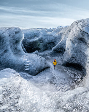 View of a figure in a yellow jacket wanders through an icy landscape of blue and white, carved by time and nature's raw power, Sveitarfelagio Hornafjordur, Iceland.