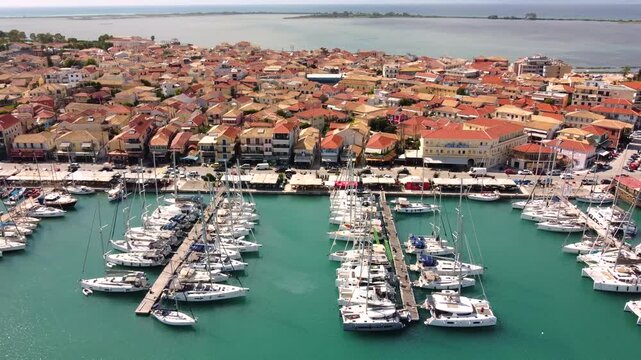 Aerial view of Lefkas Marina, Lefkada, Ionian Island in Greece. Sailboats in harbor, pedestrians and traffic moving along the promenade beside the terracotta old town, Mediterranean summer scene.