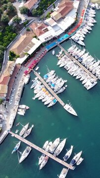 Vertical overhead view of Sivota bay, harbor with yachts and sailboats moored in turquoise Ionian waters, scenic coastal village and summer marina lifestyle, Lefkada, Greece.