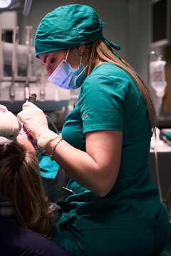 Dentist in green scrubs wearing mask and gloves treating a patient in dental clinic