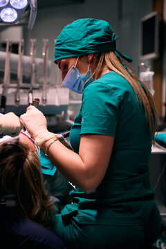 Female dentist performing dental treatment on adult patient in modern dental clinic wearing scrubs and mask