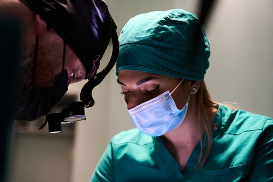 Surgical team focused on procedure in operating room with nurse and surgeon wearing masks