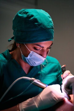 Female dentist performing focused dental procedure on patient wearing mask and green scrubs in clinic