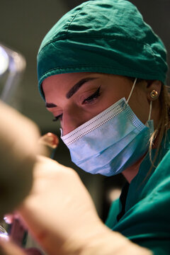 Focused female surgeon wearing surgical mask and cap performing a delicate procedure in operating room