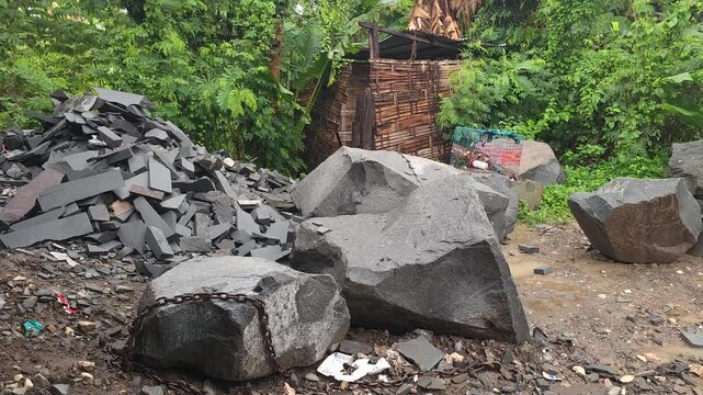 Piles of shattered slate and large extracted boulders sit haphazardly amidst lush tropical foliage, highlighting the stark contrast between nature and unregulated resource extraction.