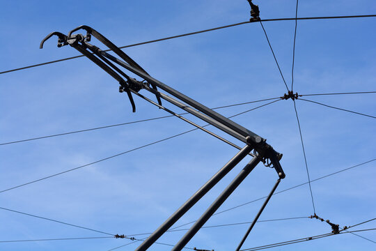 Close up of a black tram pantograph connected to overhead electric power lines against a clear blue sky