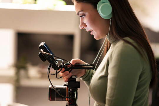 A young woman wearing headphones operates a video camera with a monitor attached, focusing on her work.