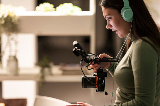 A young woman wearing headphones operates a camera with a microphone attached, focused on her work.