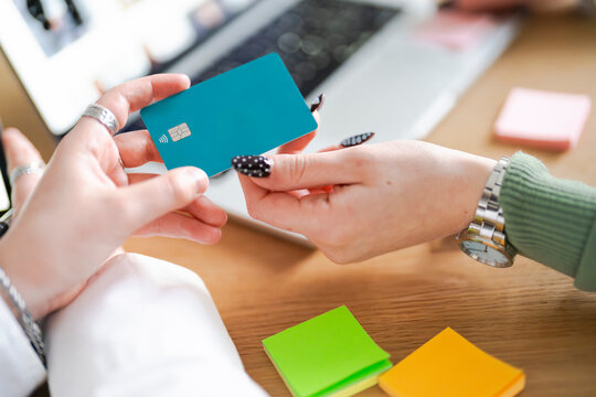 A person holds a credit card near a laptop, with sticky notes and a watch on the desk, suggesting online shopping or financial management.