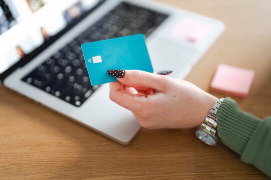A person holds a credit card near a laptop, ready for online payment or transaction.