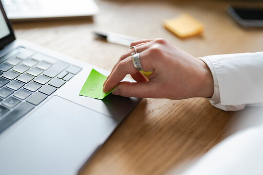 A person's hand with rings touches a green sticky note with the word "CALL" written on it, placed on a laptop keyboard.