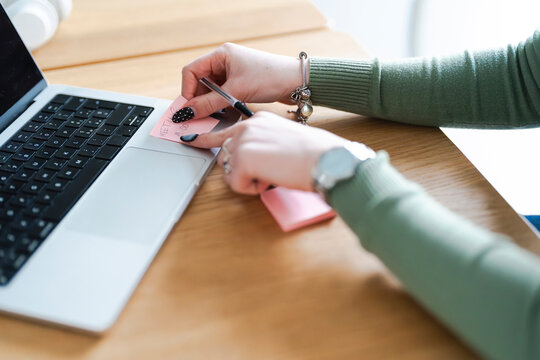 A person's hands are shown at a desk, with a laptop and a pink sticky note that reads "MEETING 19:00".