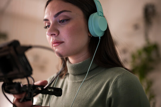A young woman wearing headphones is focused on a microphone, preparing to record audio or a podcast.