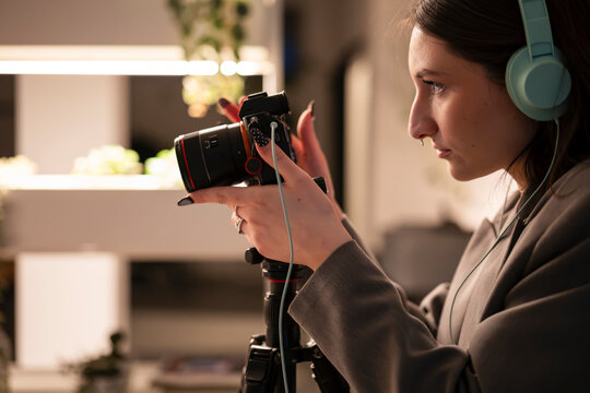 A young woman wearing headphones operates a camera on a tripod, focusing on her creative work.