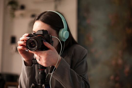 A young woman wearing headphones holds a camera on a tripod, focusing on her subject.