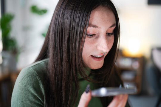 A young woman with dark hair and a nose ring looks down at her phone, smiling as she reads a message.