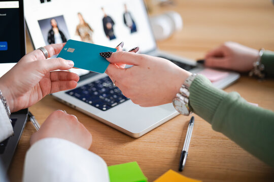 A person holds a debit card near a laptop, ready to make an online purchase. The screen displays fashion items, suggesting a shopping transaction.