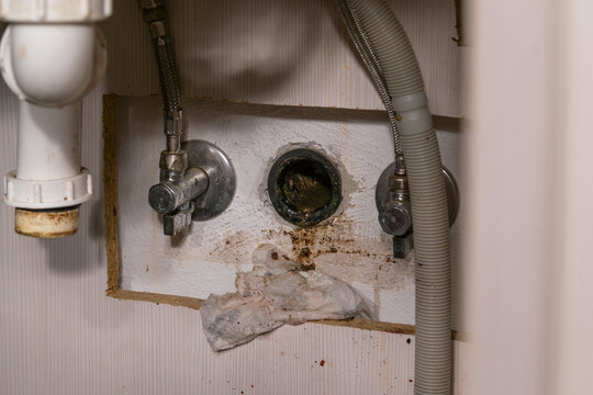 Open wall sewage drain pipe under kitchen sink with signs of clog and grease.