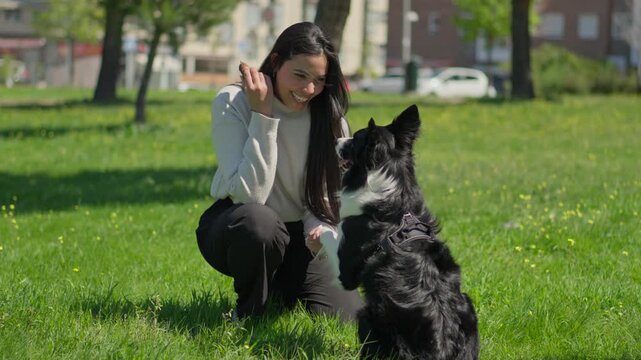 Beautiful woman smiling while training her smart border collie to give both paws in a park