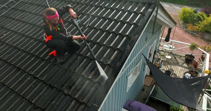 Aerial view around a female worker power washing dirt from a house roof