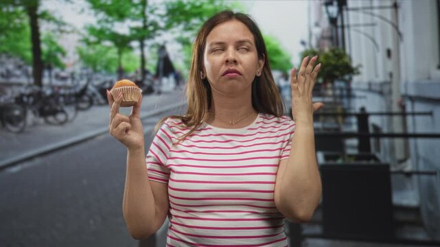 Woman holding muffin in street with raised fist, grimace, eye roll and pursed lips; disgust food aversion.