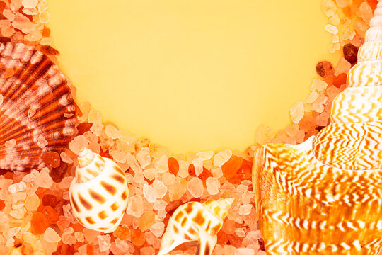 Pink Himalayan salt crystals and sea shells on yellow background with copy space