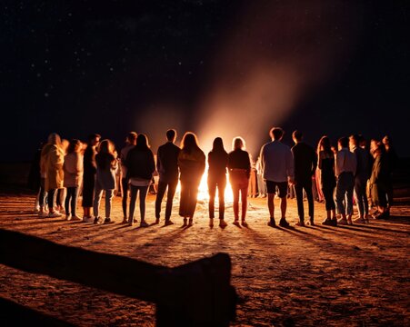 Group of people standing in a circle around a burning bonfire at night in a rural field for a community gathering event with warm amber light and a starry sky background