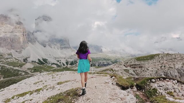 Tracking aerial pov female fit hiker hike explores iconic Tre Cime di Lavaredo in Italy Dolomites. Mountain trail breathtaking views of the three legendary limestone peaks. UNESCO World Heritage site