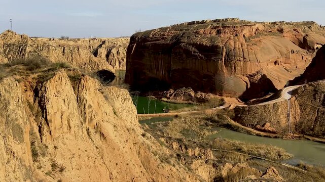High angle wide shot of winding river and lush green fields nestled between massive red sandstone cliffs and loess plateaus 