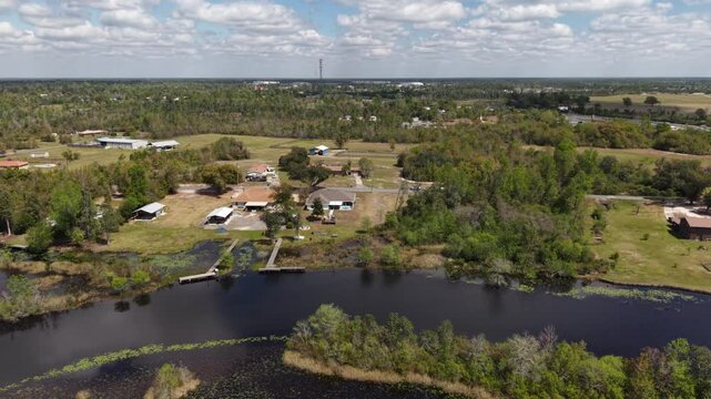 Wide aerial countryside shot of open green fields with scattered rural houses near river channel at 30A area, Florida, USA