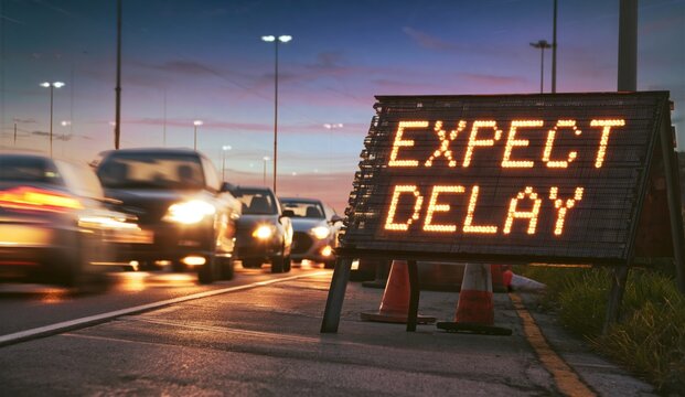 Road traffic at dusk with an electronic sign warning drivers to expect delays and slow movement ahead.