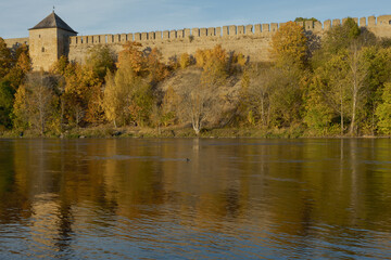 Obraz premium Historic stone fortress on river bank in autumn. Medieval architecture with towers and walls, scenic landscape with water reflection.