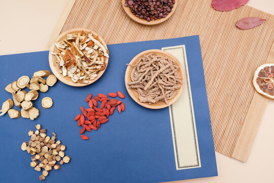 Traditional Chinese medicinal herbs including goji berries, astragalus, angelica, and other dried ingredients arranged on a blue paper background with bamboo mat
