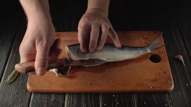 Hands of a person skillfully filleting a fish on a wooden cutting board, showcasing the process of preparing fresh seafood in a kitchen setting