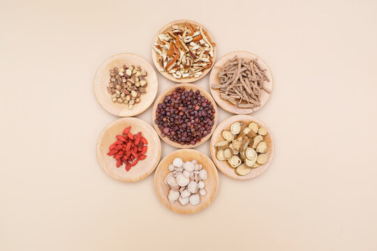 Seven types of traditional Chinese medicinal herbs displayed in small wooden dishes arranged in a circular pattern