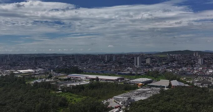 4K drone view of Leon Feffer Park in Mogi das Cruzes, Brazil, showing forest, lake and urban surroundings under blue sky and clouds.