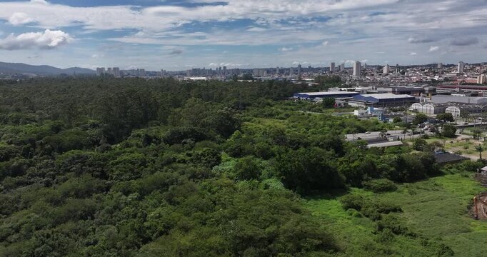 4K drone view of Leon Feffer Park in Mogi das Cruzes, Brazil, showing forest, lake and urban surroundings under blue sky and clouds.