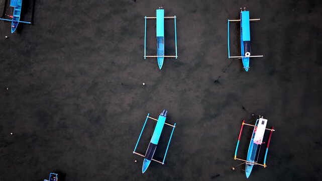 Aerial Top Down View of Traditional Jukung Outrigger Boats Moored in Calm Sea Water at Bali Beach