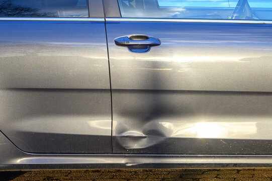 Close-up of a dented car door with scratches and reflections