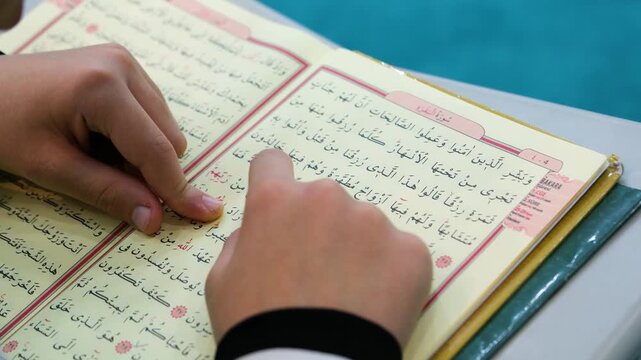 Close up of a teacher and a student's hands pointing at the holy Quran during a religious tajweed lesson for learning to read and recite the sacred text correctly indoors