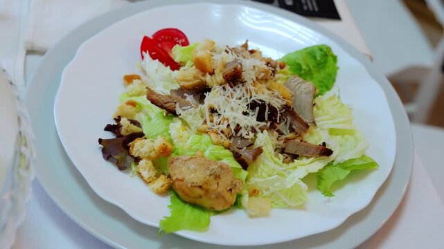 Grilled chicken caesar salad presenting crispy croutons, grated parmesan, ripe tomato slice atop fresh lettuce against pristine white surface