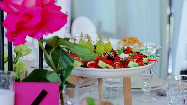 Elegant white plate displaying artfully arranged colorful canapes near delicate pink rose, presenting gourmet appetizer styling on decorated surface