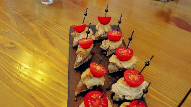 Gourmet triangular canapes spreading creamy pate, garnishing cherry tomatoes with red pepper flakes, resting on black slate against warm wooden surface
