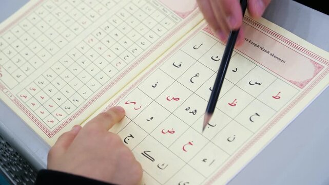 Close up of a teacher's hand pointing with a pencil at religious Arabic text while teaching a young boy how to read the Quran at a mosque school for tajweed lessons