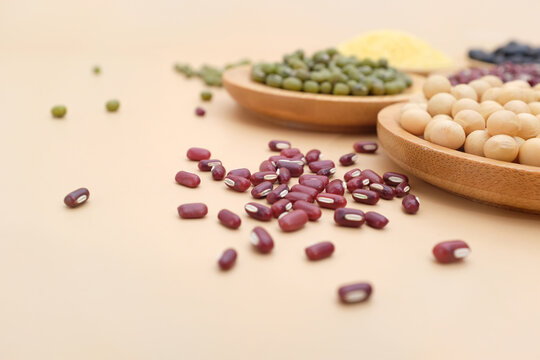 Various types of beans displayed in wooden bowls with scattered grains on a light background