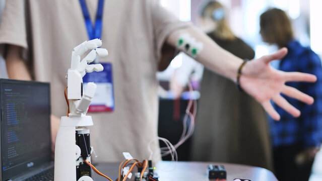 A person controls an artificial robotic arm via wires on their hand.