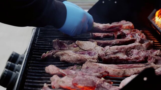 Professional chef carefully placing seasoned rosemary and garlic rubbed ribs on sizzling barbecue grill, methodically turning meat to achieve perfect even char and caramelization